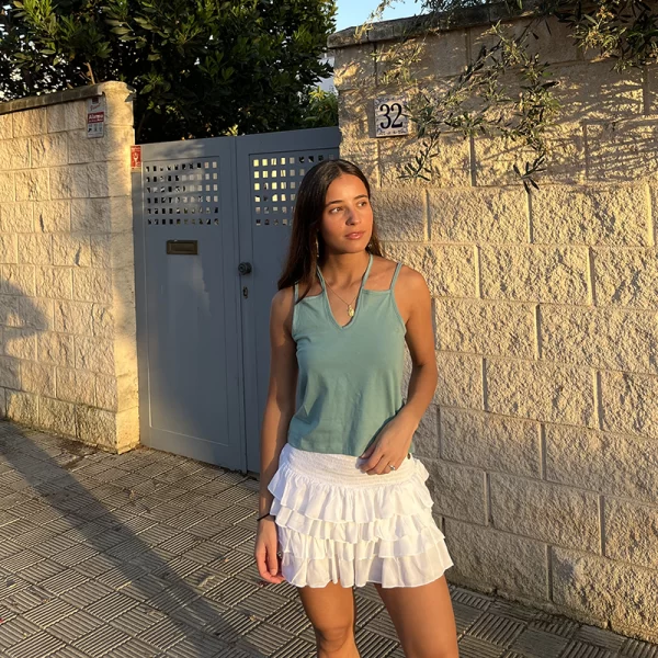 chica posando con un top verde de tirantes dobles y Falda pantalón blanca con cuatro volantes, fruncido con gomas elásticas en cintura y short interior de punto liso a tono.