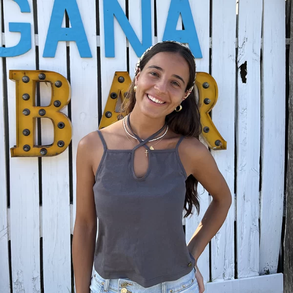 chica posando sonriendo con un top gris antracita de tirates con cordón para anudar al cuello y mini falda tejana azul con tachuelas