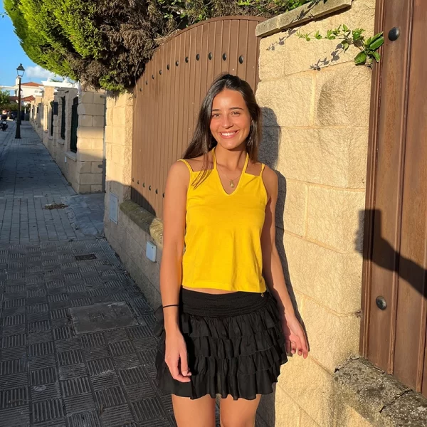 chica sonriendo con una camiseta de tirantes dobles en amarillo y una falda corta pantalón con 4 volantes en negra