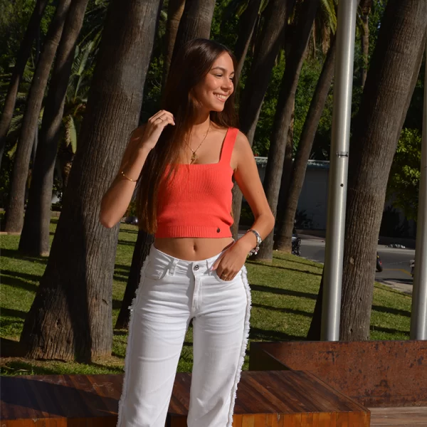 chica posando con un top coral anaranjado de tricotosa y tirantes con un pantalón largo blanco con flecos en las costuras laterales