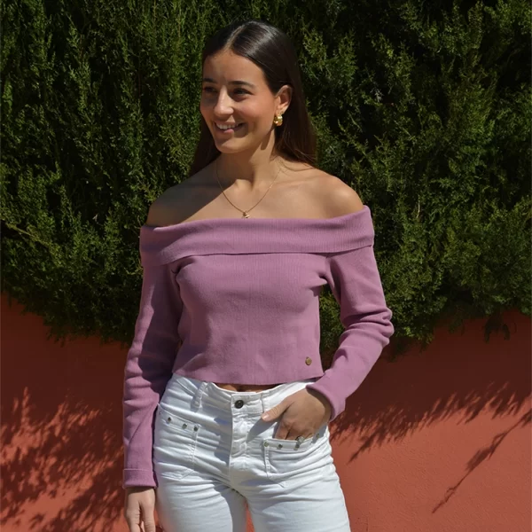 chica sonriendo con una mano en el bolsillo de su pantalón tejano blanco con bolsillos frontales con tachuelas plateadas y Top de punto rosa con hombros descubiertos con vuelta en tejido 52% Viscosa, 46% Algodón, 2% Elastán