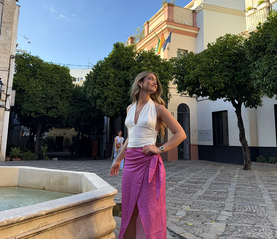 chica paseando por una plaza de Sevilla con un top blanco con espalda al aire y falda pareo estampada en tonos rosas y lilas