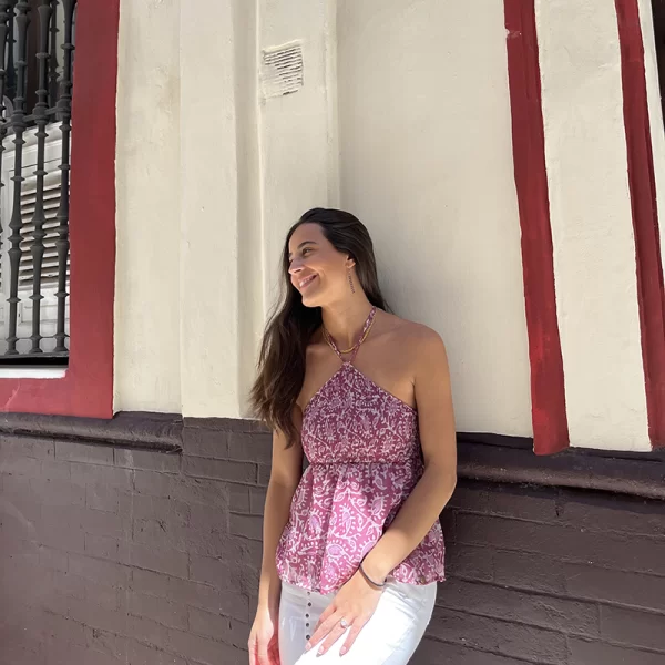 chica morena apoyada en una fachada con un top anudado al cuelo con estampado floral en tonos rosas y beige