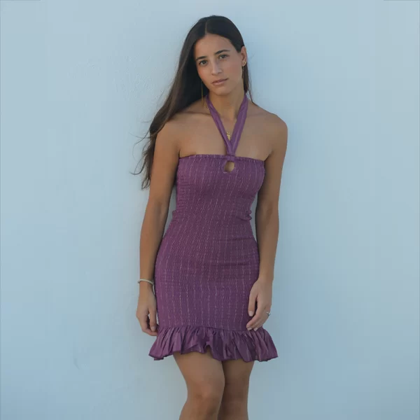 chica apoyada en una pared con un vestido fruncido en color berenjena con cuello halter y hilo de lurex plateados