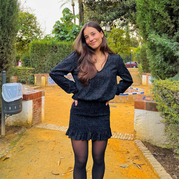 Chica joven con pelo castaño que viste un vestido estampado color negro con print en turquesa y marrón. Fruncido con gomas elásticas en la parte de la falda y en puños.