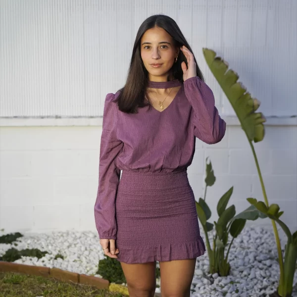 chica con vestido berenjena con tejido fantasía con detalles bordados, fruncido en la parte de la falda y cuello choker con cierre de botón en cuello. Con forro en interior de cuerpo y falda. 