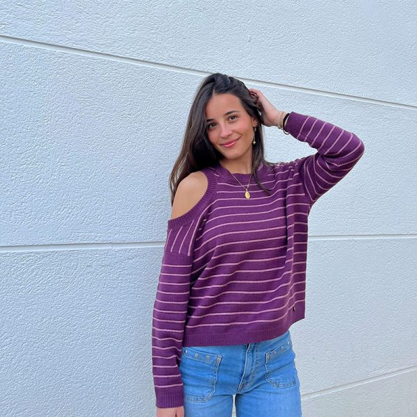chica sonriendo delante de una pared blanca con un jersey de rayas morado con hilo de lúrex muy discreto en morado. Hombro derecho descubierto